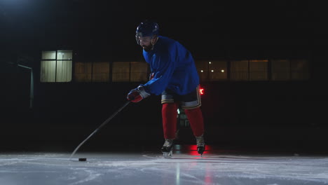 Man-hockey-player-with-a-puck-on-the-ice-in-hockey-form-leaves-with-a-stick-in-his-hands-out-of-the-darkness-and-looks-straight-into-the-camera